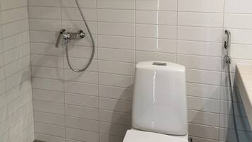 Um banheiro com paredes em azulejo branco, chuveiro com um chuveiro manual, vaso sanitário e uma prateleira com toalha.