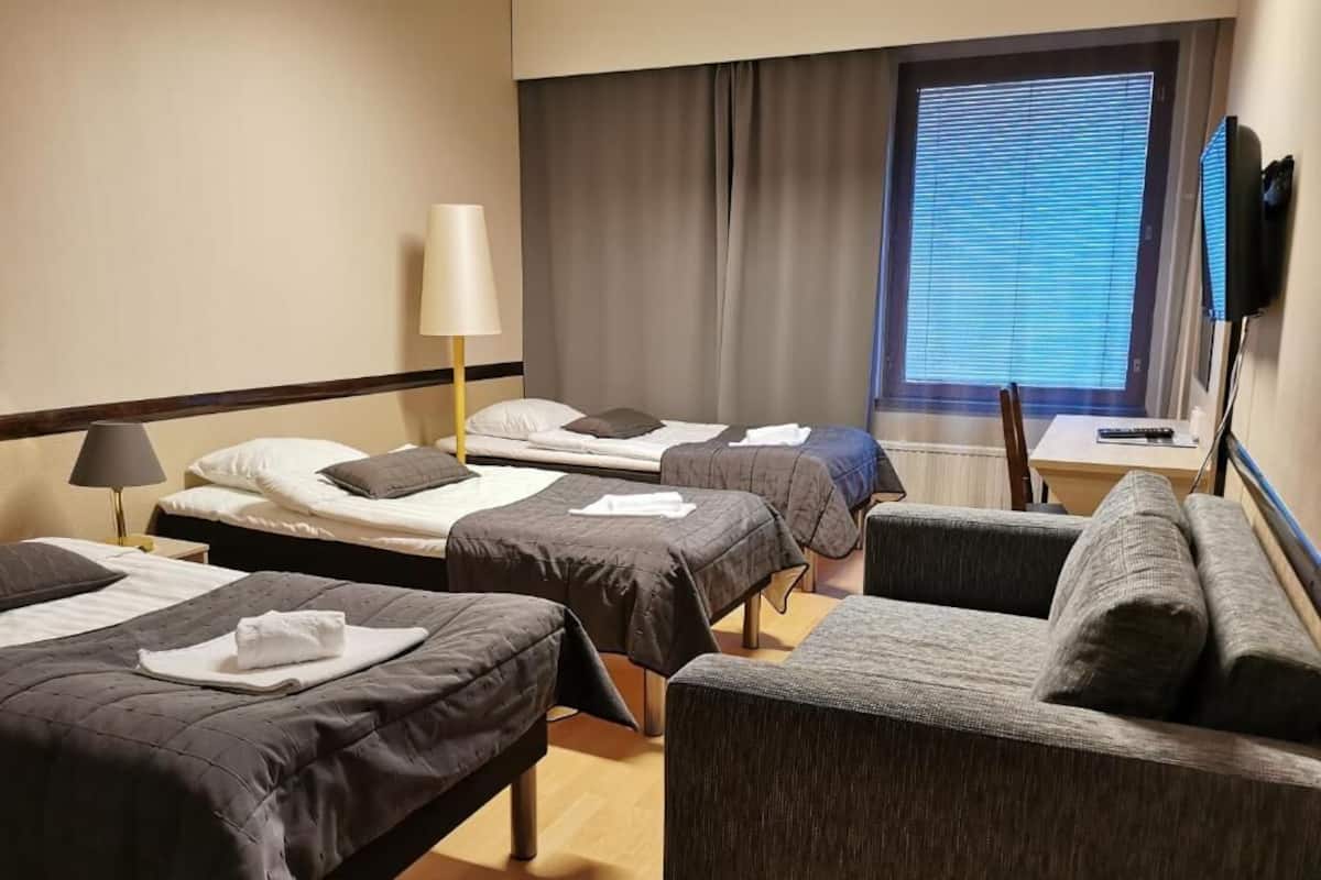 Een hotelkamer met twee eenpersoonsbedden, een bank, een televisie en een raam met zonwering.