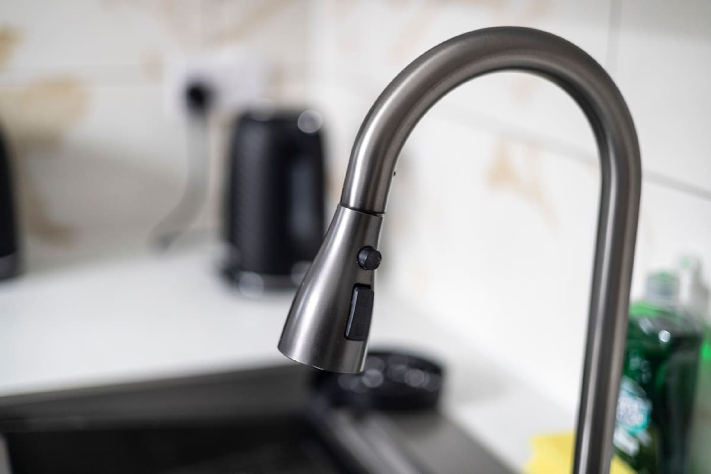A modern kitchen with a stainless steel faucet, a kettle, and a green bottle on the counter.