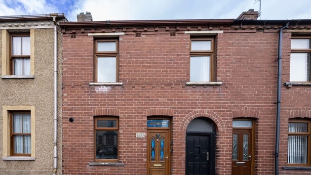 A red brick building with two windows on the ground floor and a door with a blue sign. - 3bedroom 2 Bathroom House-free Parking 5 Beds (Barrow-in-Furness)