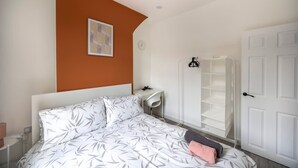 A bedroom with a bed, a bedside table, a wall clock, a framed picture, a white wardrobe, and a door. - 3bedroom 2 Bathroom House-free Parking 5 Beds (Barrow-in-Furness)