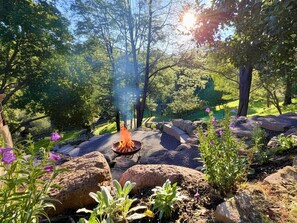 A campfire in a natural setting surrounded by rocks and greenery.