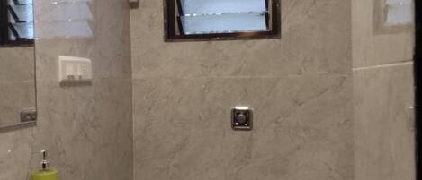 Ein Badezimmer mit einer Marmorwand, einer weißen Toilette, einem Waschbecken mit grünem Seifenspender und einem Fenster mit Jalousien.