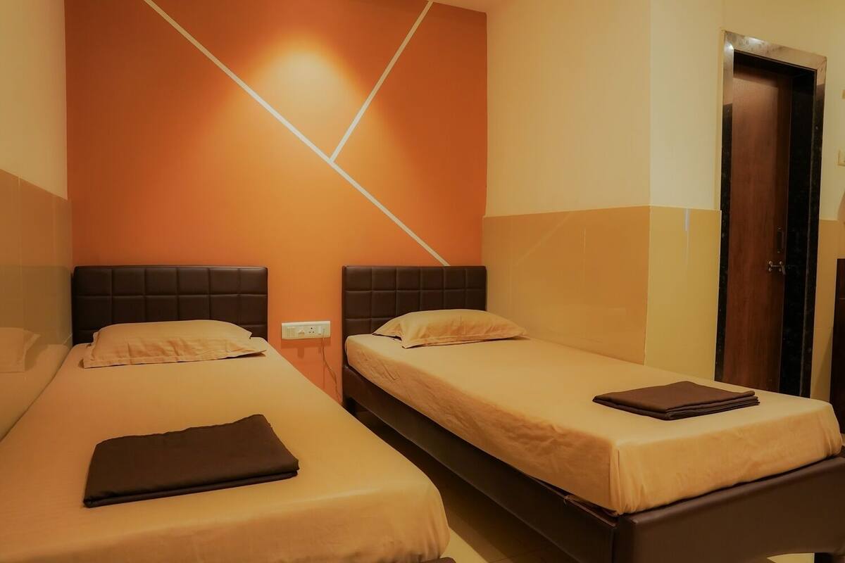 A hotel room with two single beds, a wooden door, and a wall-mounted light fixture.