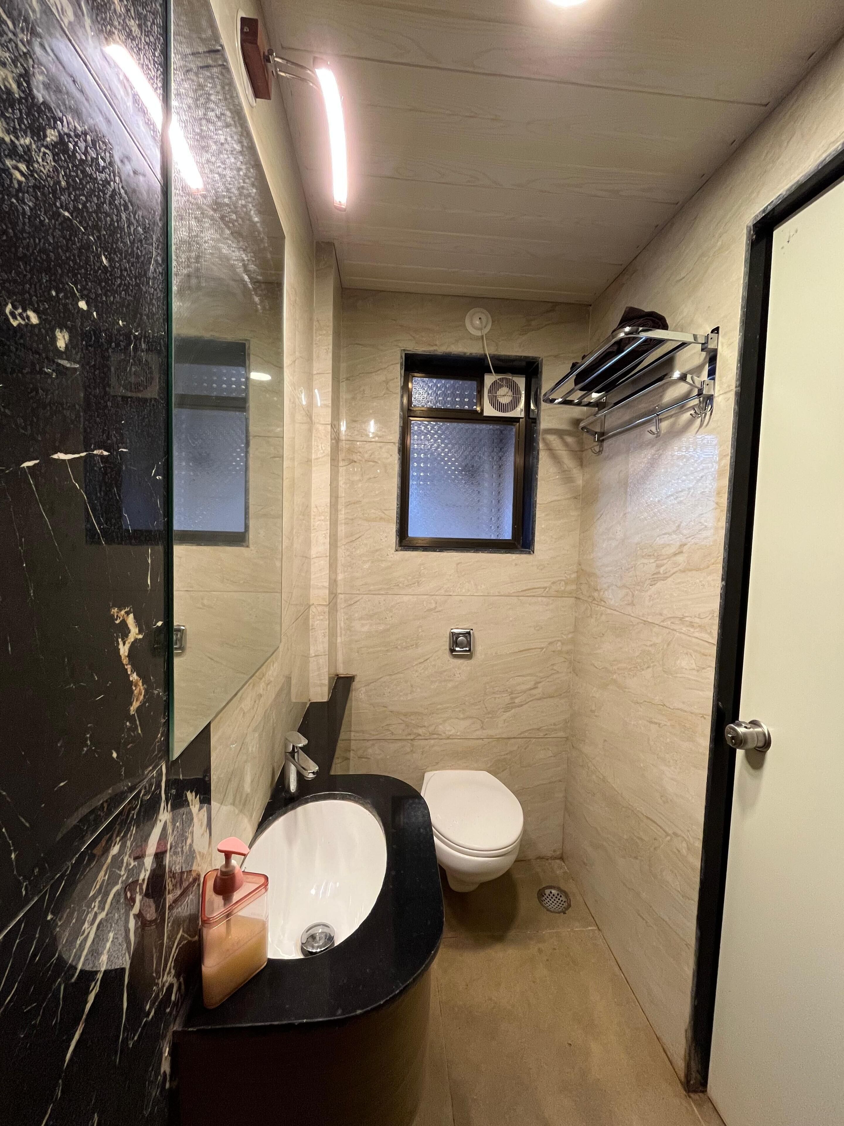 Casa de banho compacta com lavatório preto, sanita branca e uma pequena janela com um porta-toalhas.