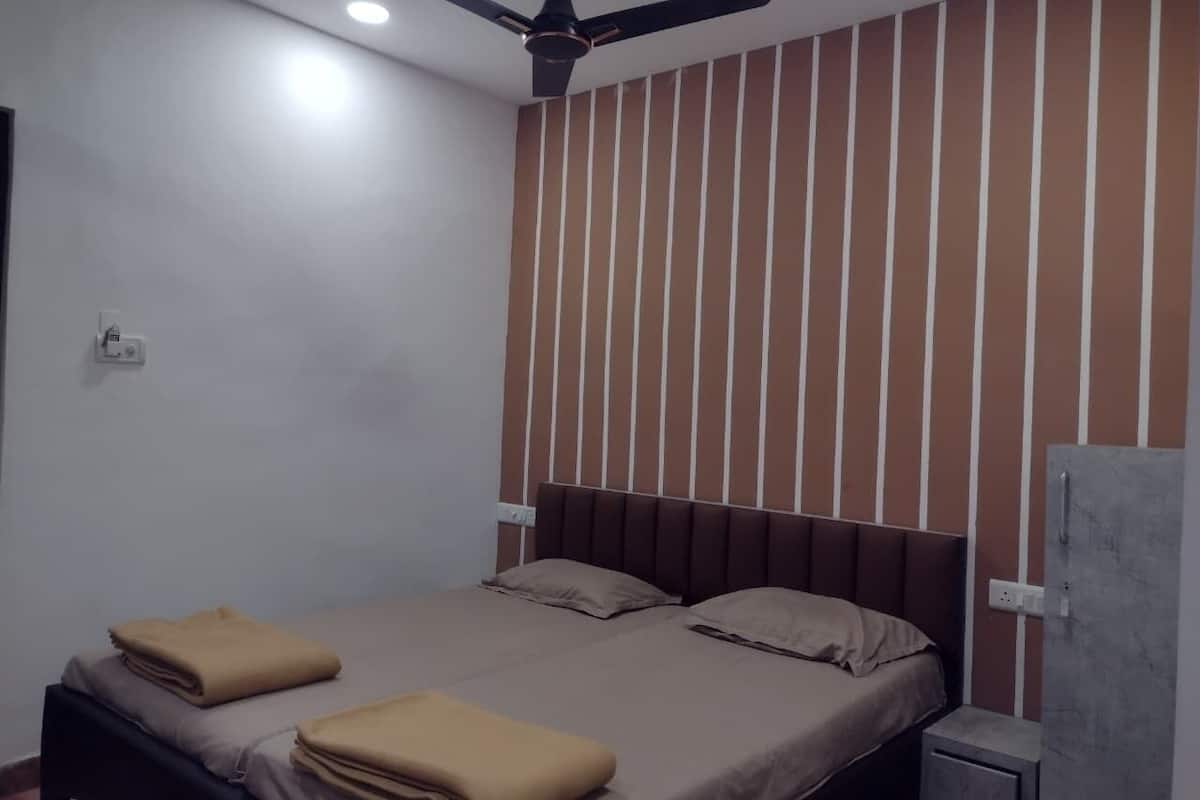 A bedroom with a bed, a ceiling fan, a nightstand, and a wall with vertical stripes.