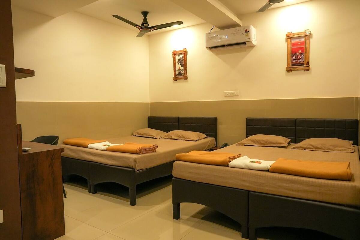 A hotel room with two beds, a desk, a ceiling fan, an air conditioning unit, and two framed pictures on the wall.