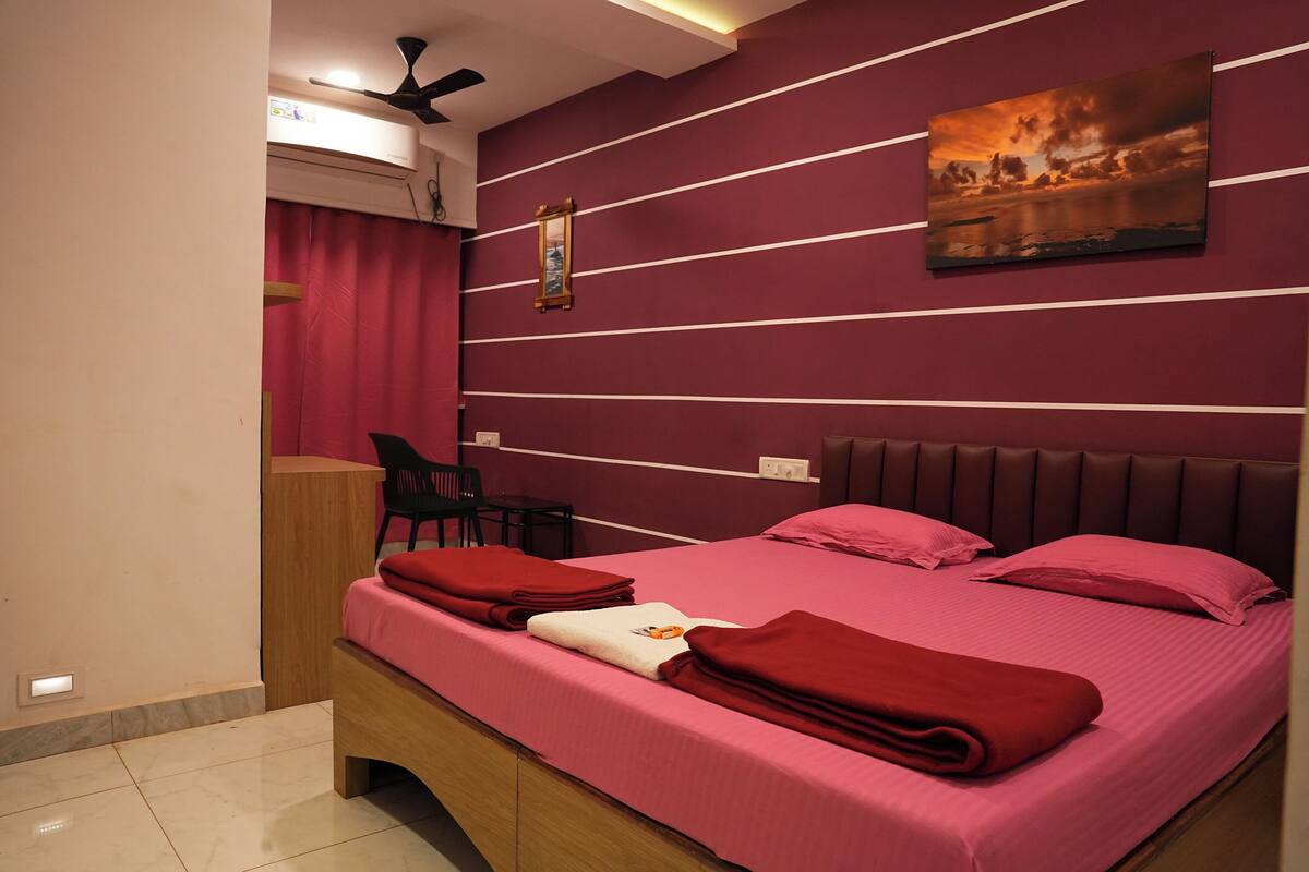 A bedroom with a bed, pillows, a bedside table, a chair, a wall-mounted picture, and a ceiling fan.