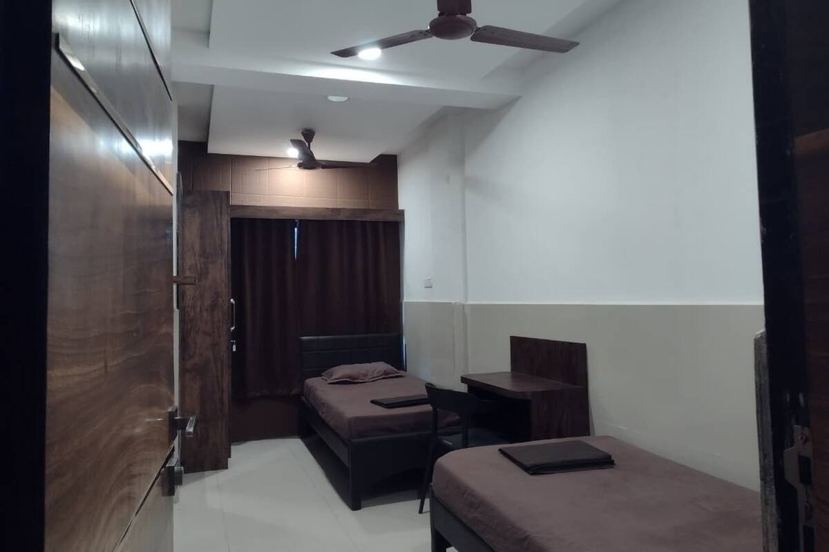 A compact room with a bed, a desk, and a chair. There is a ceiling fan and a window with curtains.