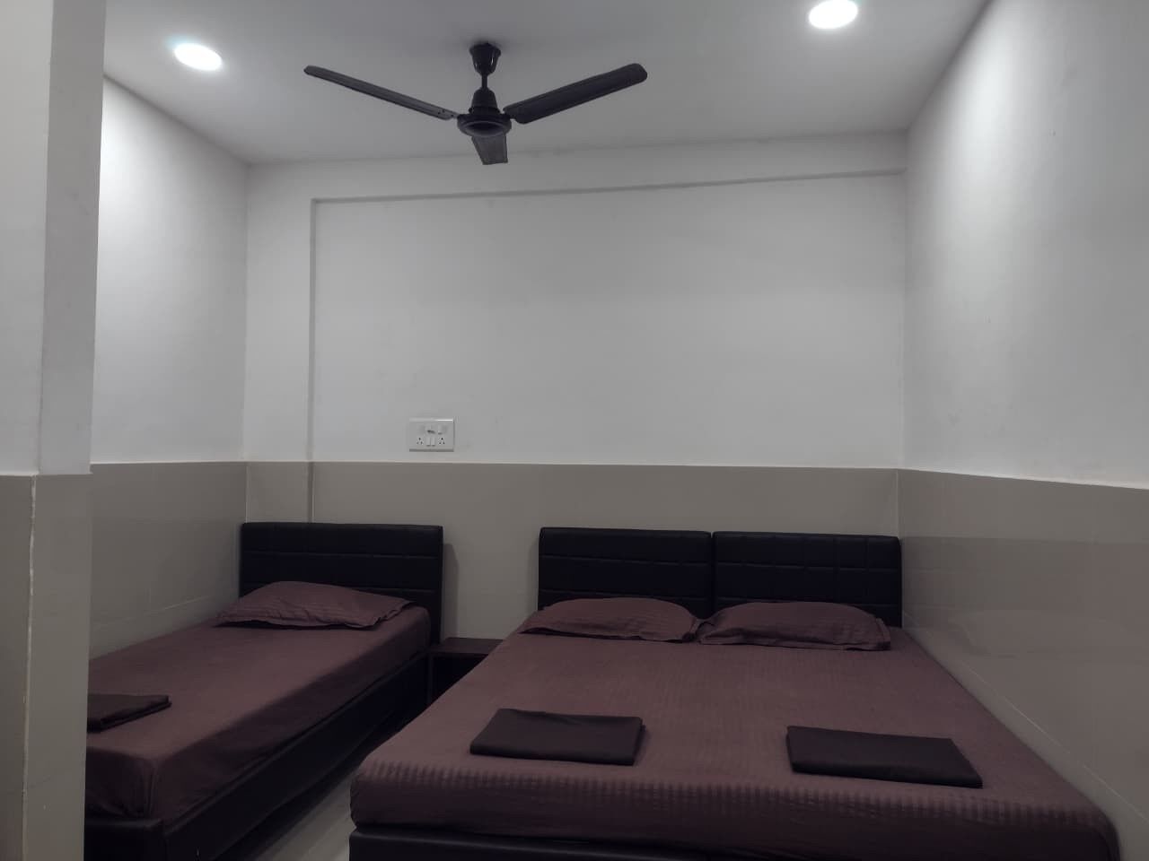 Un petit logement composé d’une seule pièce, comprenant deux lits simples, un ventilateur de plafond et un éclairage encastré.
