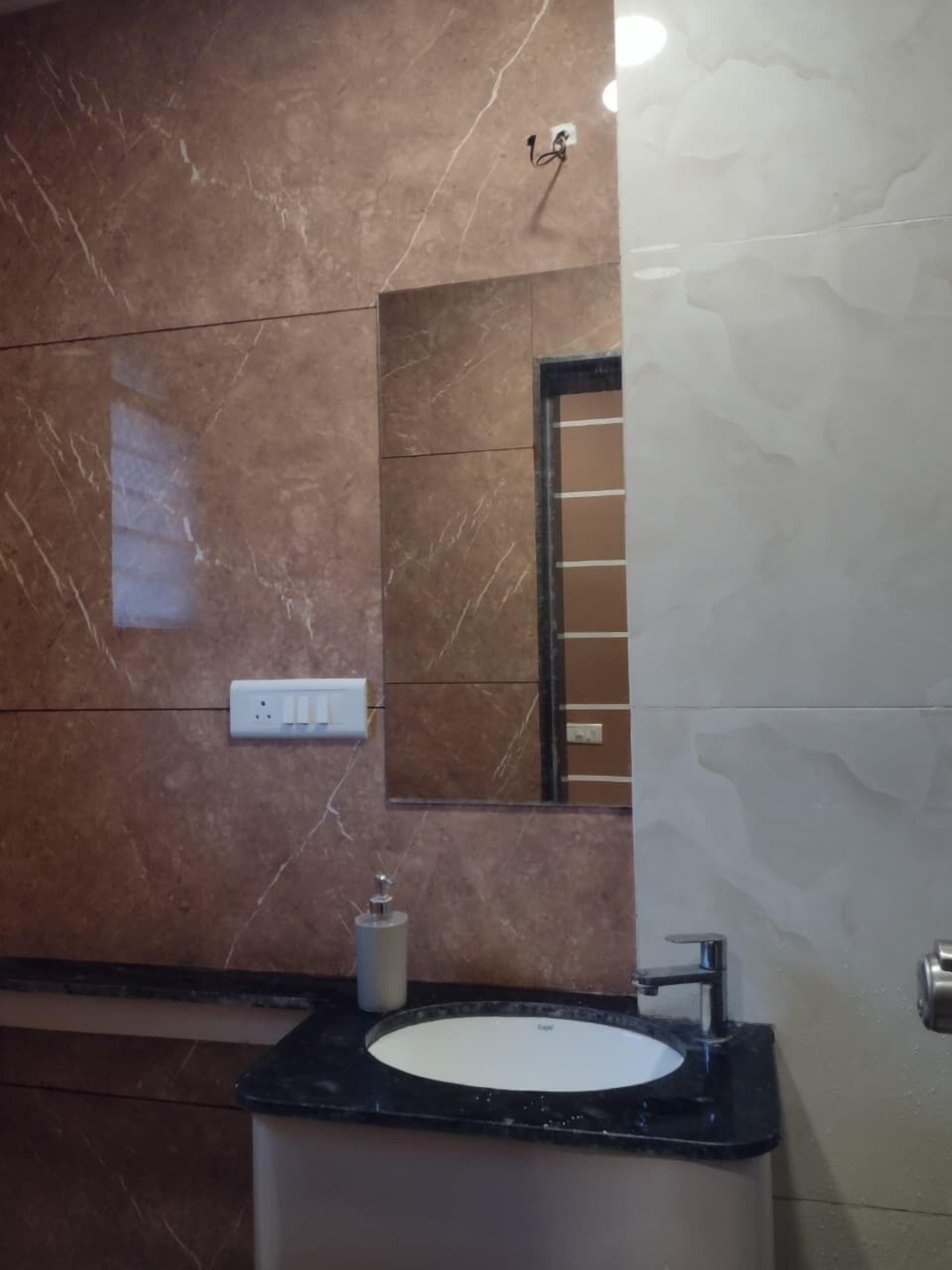 Un bagno con una parete in marmo, un lavabo con piano nero, uno specchio e un dispenser per sapone.