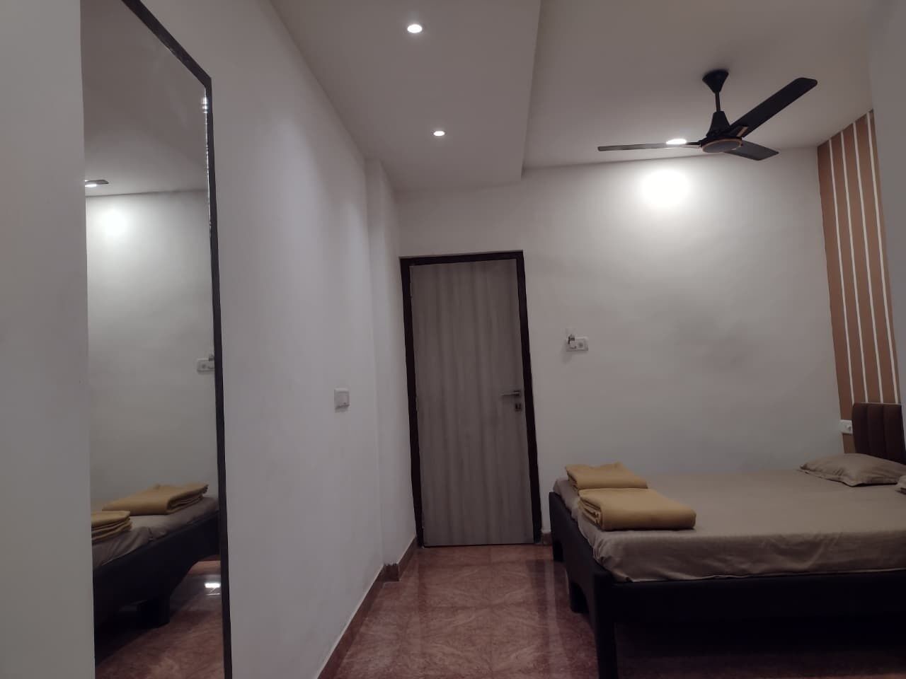 A bedroom with a bed, a ceiling fan, a door, and a mirror.