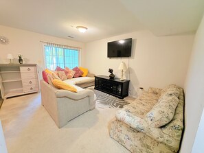 Ein Wohnzimmer mit einer Couch, einem Couchtisch, einem an der Wand befestigten Fernseher und einem Fenster mit Jalousien.