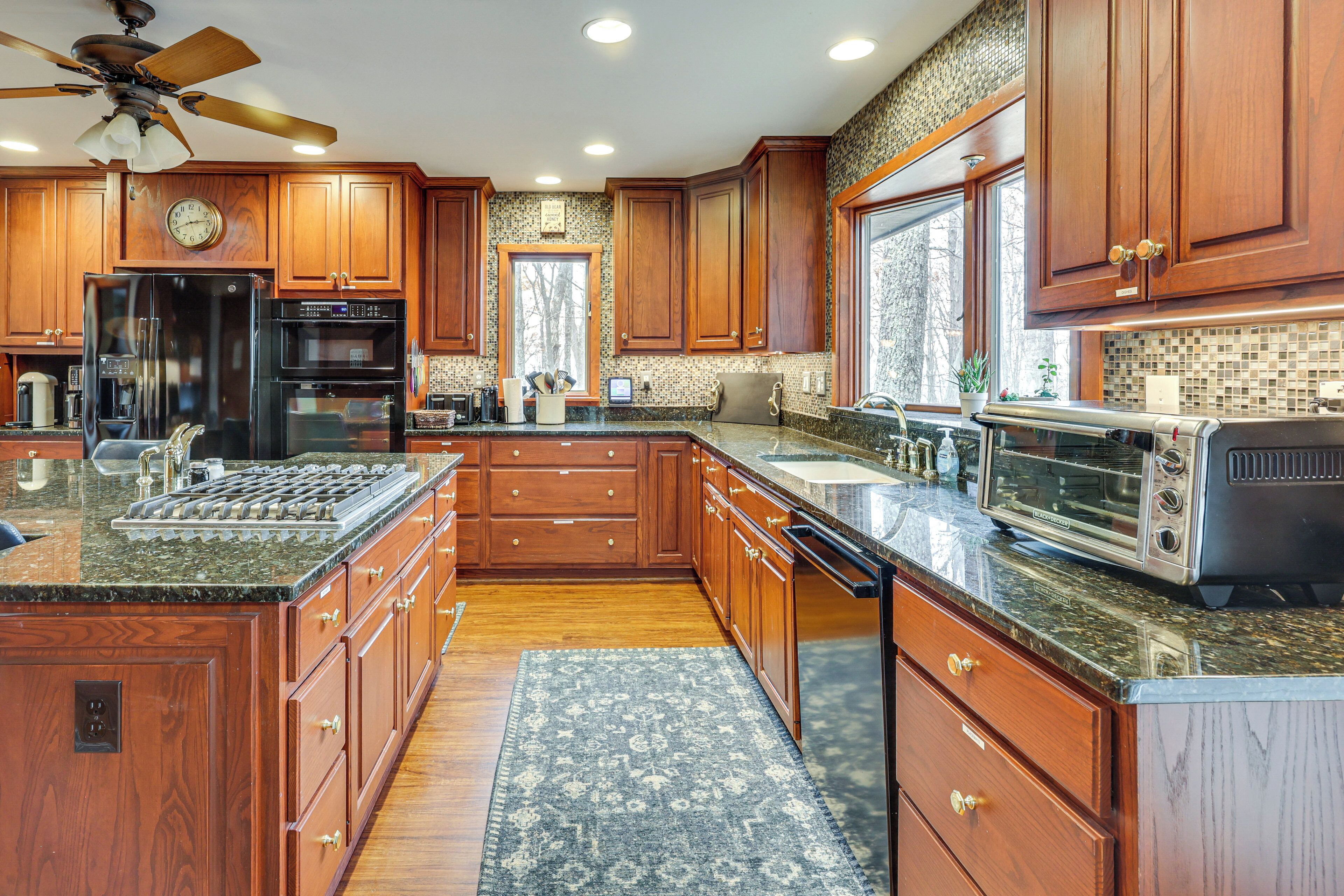 A spacious kitchen with wooden cabinets, a large island, stainless steel appliances, and a view to the outside.