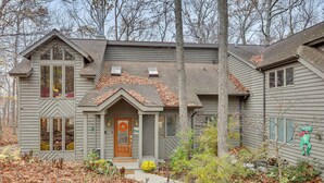 A two-story house with a front porch, a chimney, and a small garden area with a tree and shrubs. - Grand Wintergreen Resort Home w/ Hot Tub! (Nellysford)