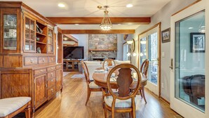 A dining area with a wooden table and chairs, a built-in cabinet, and a stone fireplace. - Grand Wintergreen Resort Home w/ Hot Tub! (Nellysford)