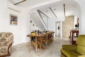 A dining area with a long table, wooden chairs, and a floral sofa.