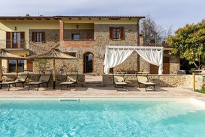 A poolside area with lounge chairs, a stone building with a balcony, and a clear pool.