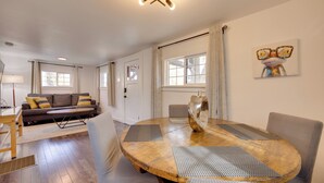 A modern living room with a round wooden dining table, grey upholstered chairs, a grey sofa with yellow cushions, and a large window with curtains. - 2 Mi to Dtwn: Colorado Springs Gem w/ Hot Tub! (Colorado Springs)