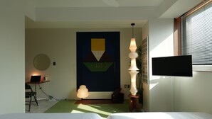Habitación de hotel con dos camas, un escritorio con una computadora portátil, un cuadro abstracto grande, una lámpara de pie alta y un televisor en la pared.
