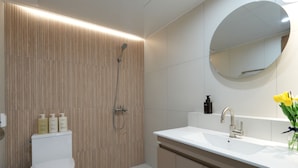 Un baño moderno con pared de paneles de madera, inodoro blanco, ducha, lavamanos con espejo y artículos de aseo en la encimera.