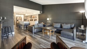 Una sala de estar moderna con un sofá gris, una mesa de centro y un comedor con taburetes de bar.