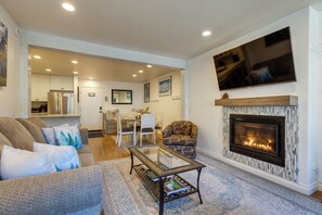 A living room with a fireplace, a sofa, a coffee table, and a television mounted on the wall. - Mammoth Mtn Ski-In/Out Condo w/ Hot Tub Access! (Mammoth Lakes)