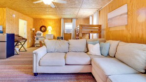 Un salon chaleureux avec un grand canapé d’angle beige, un ventilateur de plafond et un mur en bois.