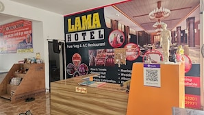 A reception desk with a sign for LAMA HOTEL, a pure veg & AC restaurant, and a QR code for booking. - Lama Hotel Barabar (Jahanabad)
