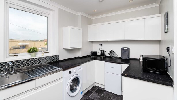 A compact kitchen with a washing machine, a microwave, and a toaster. - Spacious 3 BED House With Parking (Bo'ness)