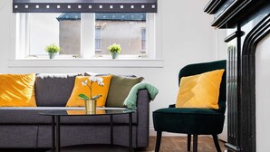 A modern living room with a grey sofa, a round coffee table, and a dark green armchair. There are two potted plants on the windowsill. - Spacious 3 BED House With Parking (Bo'ness)