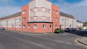 A multi-story building with a flat roof, rectangular windows, and a red and beige facade. - Spacious 3 BED House With Parking (Bo'ness)
