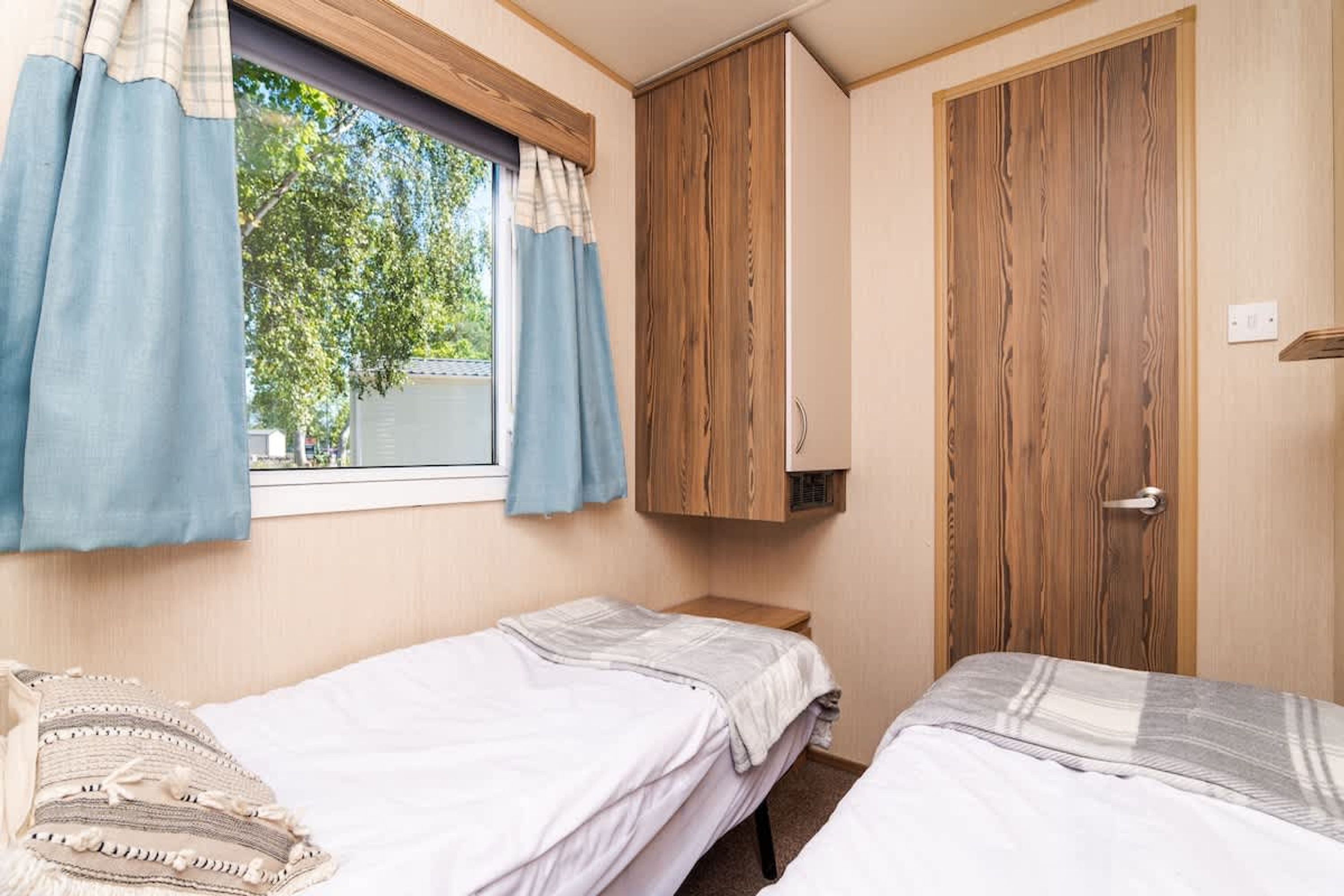 Une chambre avec deux lits, une fenêtre avec des rideaux, une armoire en bois et une petite table de chevet.