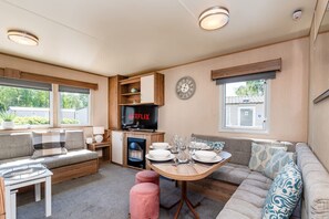 A cozy living area with a sofa, a dining table set, a television, and a clock on the wall. - 3 Bed Caravan - Seton Sands (Prestonpans)