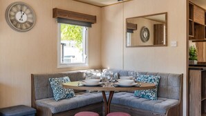 A dining area with a bench, table set for four, and a clock on the wall. - 3 Bed Caravan - Seton Sands (Prestonpans)