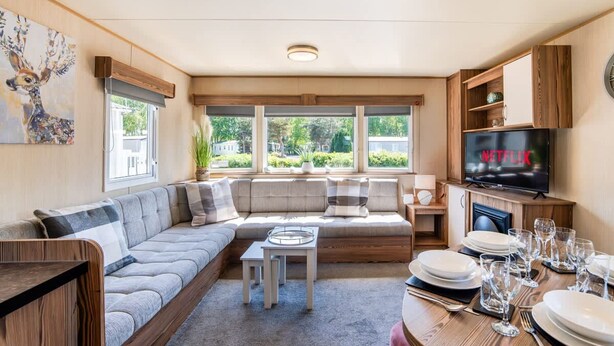 A modern living room with a sofa, a coffee table, a dining table set for four, and a television displaying 'NETFLIX'. - 3 Bed Caravan - Seton Sands (Prestonpans)
