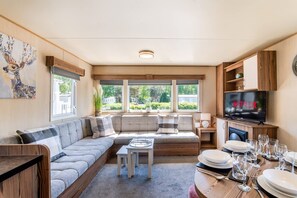 Una sala de estar moderna con un sofá, una mesa de centro, una mesa de comedor preparada para cuatro personas y un televisor que muestra 'NETFLIX'.