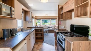 A compact kitchen with a stove, microwave, and wooden cabinets. - 3 Bed Caravan - Seton Sands (Prestonpans)