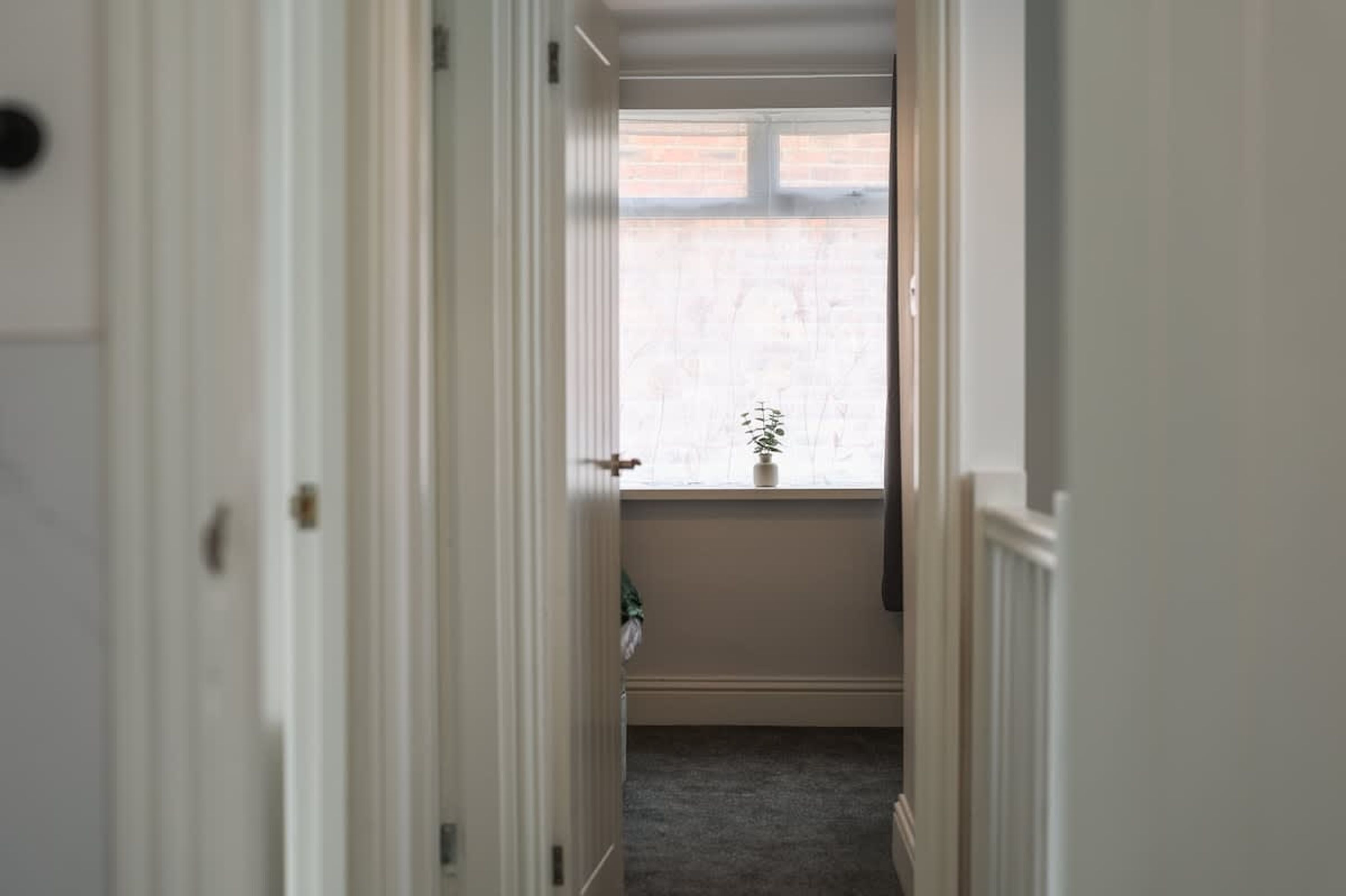 Ein schmaler Flur mit einem Fenster am Ende, einer Tür links und einer Pflanze auf der Fensterbank.