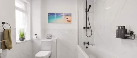 A modern bathroom with a toilet, a shower, and a bathtub. There is a window with a towel hanging on the door, a potted plant, and a picture on the wall.