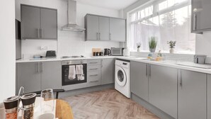 A modern kitchen with grey cabinets, a built-in oven, a washing machine, and a window with a view of trees. - 3 Bedroom House With Free Parking (Durham)