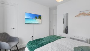 A bedroom with a bed, a chair, a TV on the wall, a mirror, and a radiator. - 3 Bedroom House With Free Parking (Durham)