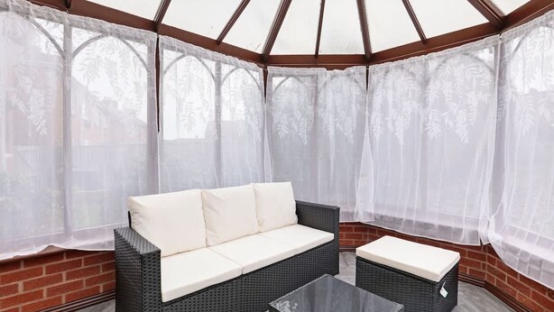 A covered patio area with a wicker sofa and a matching ottoman, a glass coffee table, and a brick wall. - 3 Bedroom House With Free Parking (Durham)