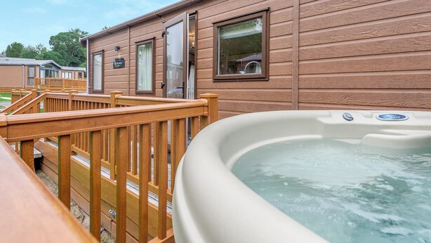 A wooden cabin with a hot tub, wooden deck, and a window with a view. - Superb and spacious lodge with one double, one twin and one single. (Bala,)