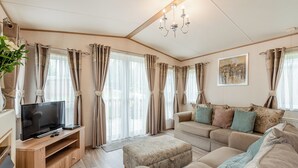 A living room with a sofa, ottoman, TV, and curtains. - Superb and spacious lodge with one double, one twin and one single. (Bala,)