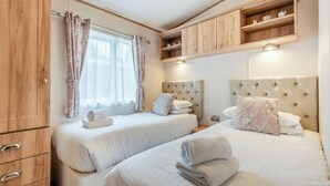 A hotel room with two beds, wooden cabinets, a window with curtains, and a built-in shelf above the beds. - Superb and spacious lodge with one double, one twin and one single. (Bala,)