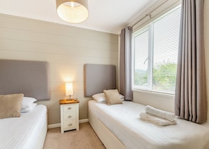 A hotel room with two beds, a bedside table with a lamp, a window with blinds, and a view of greenery outside. - 1 bedroom accommodation in Bala, (Bala,)