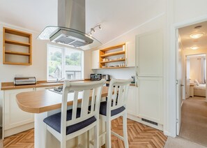 A modern kitchen with white cabinetry, a wooden countertop, a built-in stove, and a window with blinds. - 3 bedroom accommodation in Bala, (Bala,)