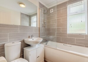 A modern bathroom with a white sink, toilet, and bathtub, featuring a tiled wall and a window. - 1 bedroom accommodation in Bala, (Bala,)