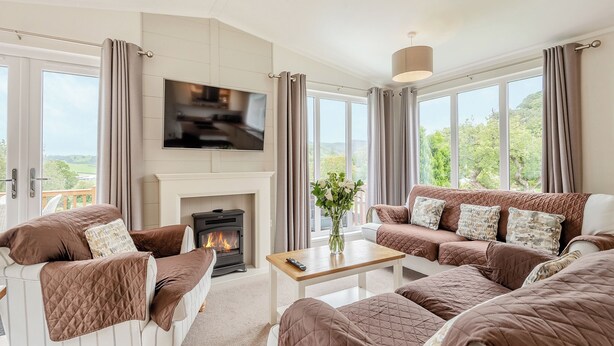 Ein modernes Wohnzimmer mit Kamin, Flachbildfernseher und großen Fenstern mit Blick ins Freie.